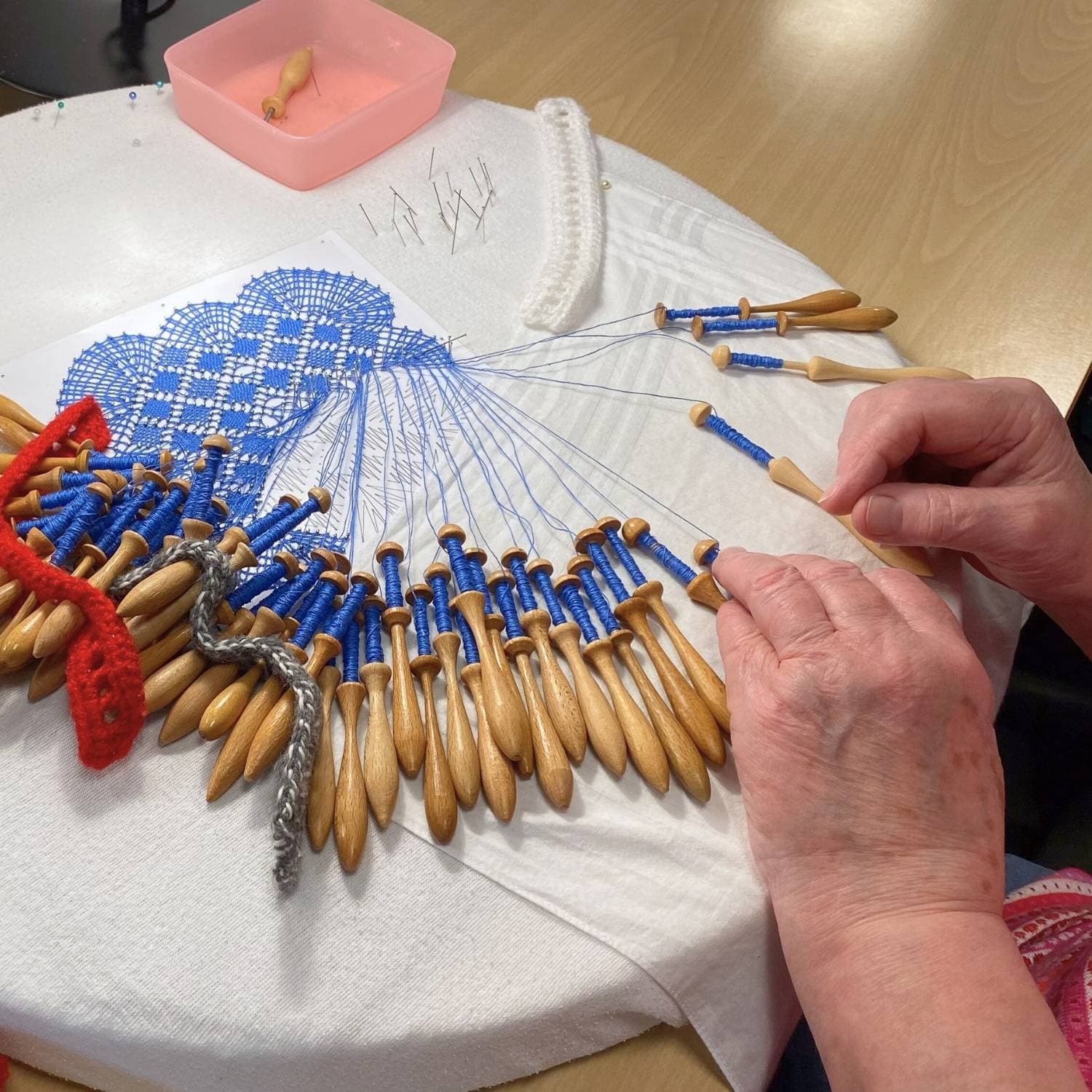 Kursist der knipler på et kniplebræt med blå tråd