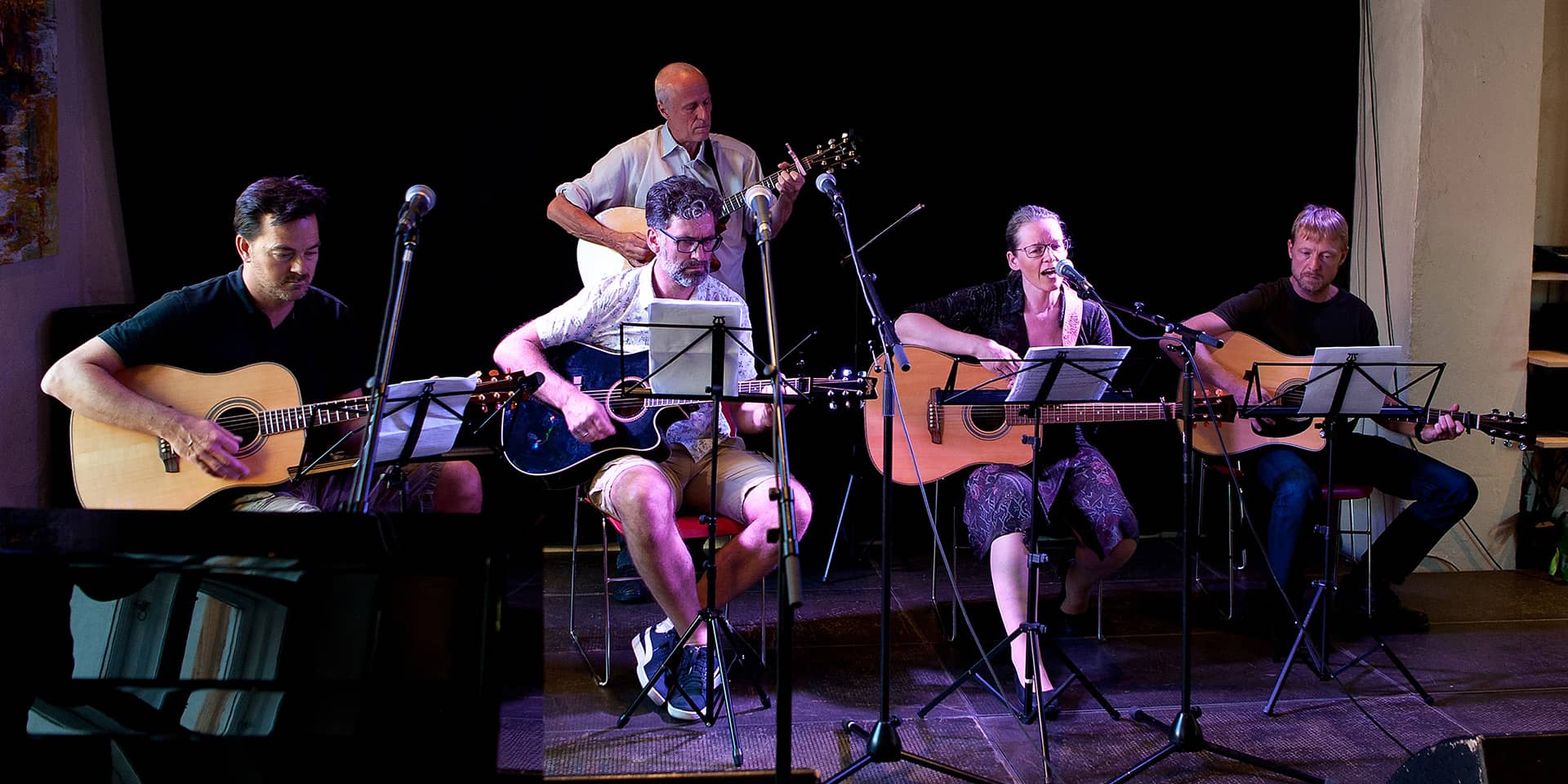 Mennesker, der sidder på skamler med guitarer i et mørkt rum med skarpt lys til musikkursus i FOF Aarhus, guitar øvede.
