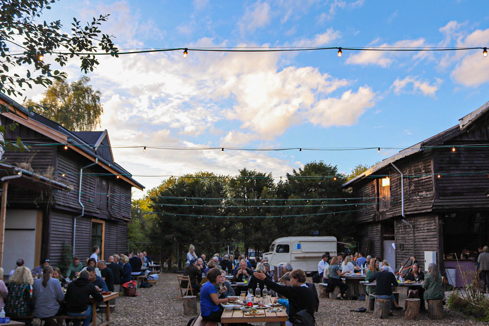 Foto af Jernbanebyen med gamle værkstedsbygninger og folk, der sidder bænket og spiser.