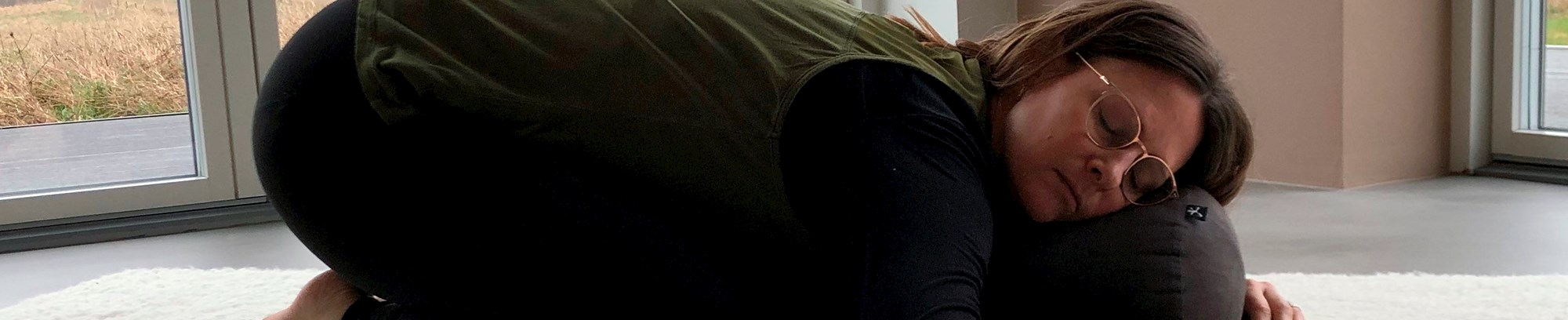 Yin yoga underviser, Malene Lillebæk Clausen, der laver øvelsen "Barnet" på en yogamåtte med en yogapølle